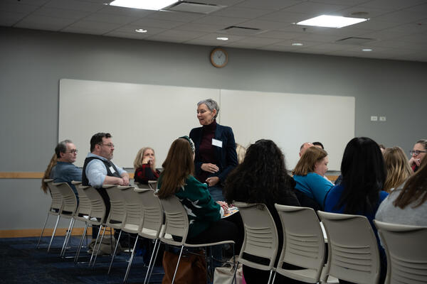 Attendees sit in a row of chairs and listen as one of their colleagues speaks.